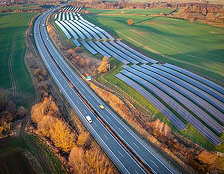 Photo of a freeway cutting through a landscape of green rolling hills with a solar farm running alongside the right side of the road.