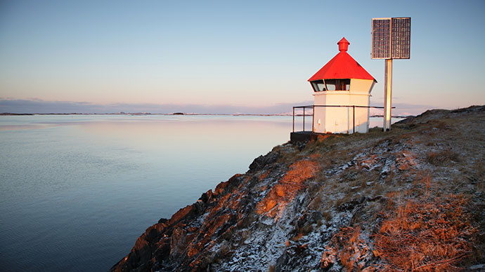 Winter photo of a lighthouse with a red roof by the sea powered by a solar panel.