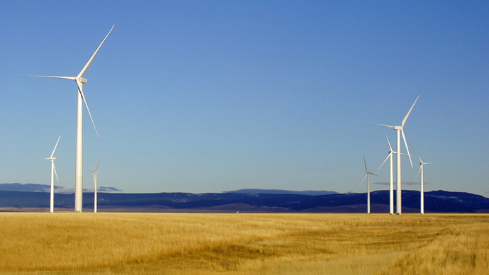 Wind turbines in a yellow field with a blue sky.