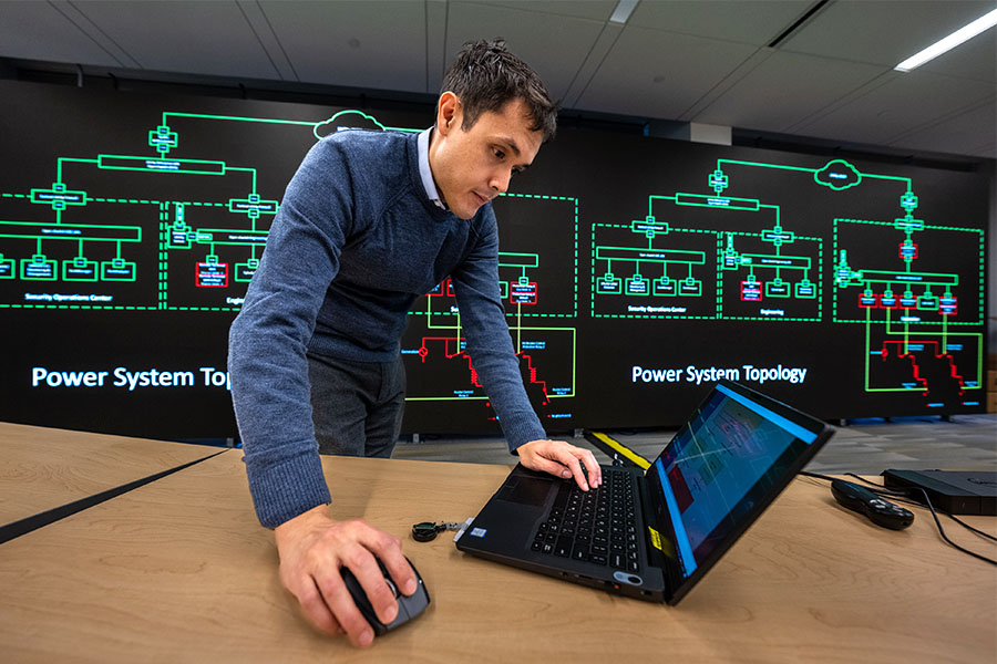 Man working on laptop with power system topology projection in background.