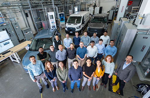 People stand in front of electric vehicles inside lab