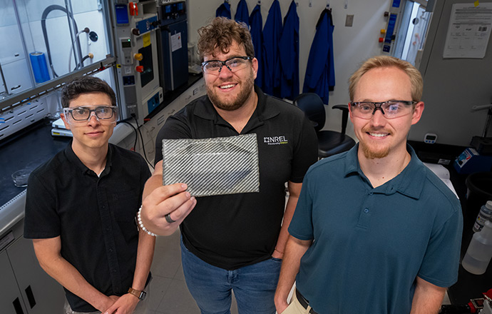 Three people in a lab with one person holding up a thermoformed section of carbon fiber composite.