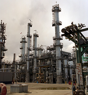 Photo of a petroleum refinery showing  multiple large columns with ladders and scaffolding and a series of interconnected pipelines