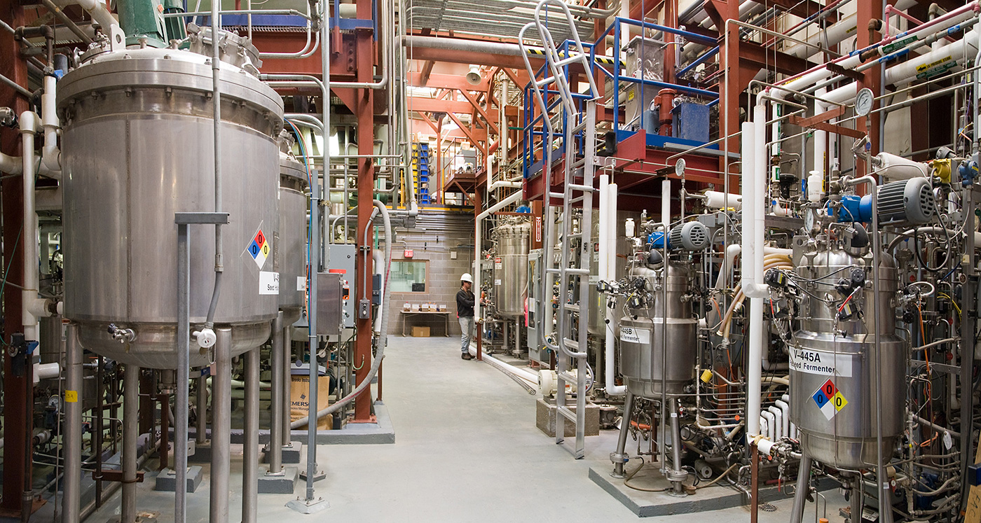 Photo of NRELs Biochemical Process Development Unit showing a series of metal tanks, scaffolding, tubes, and pipes on multiple levels within a facility.