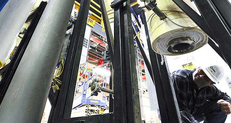Photo of a man kneeling and looking underneath large, testing  equipment in an NREL facility.