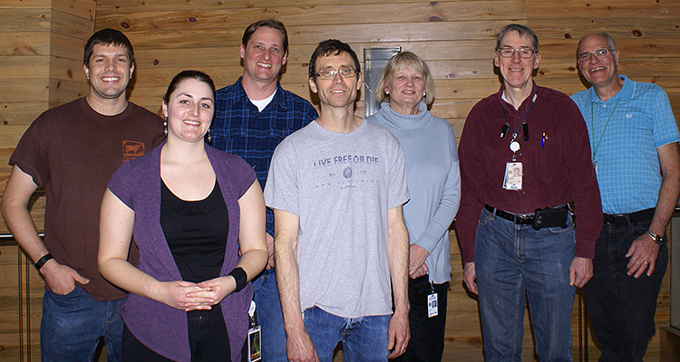 Photo of a group of smiling men and women posing in a casual office setting.