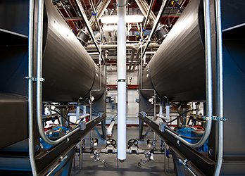 Photo of two high-solids enzymatic hydrolysis reactors (large metal tubes) that are staged to accept a continuous stream of pretreated biomass for semi-continuous processing.