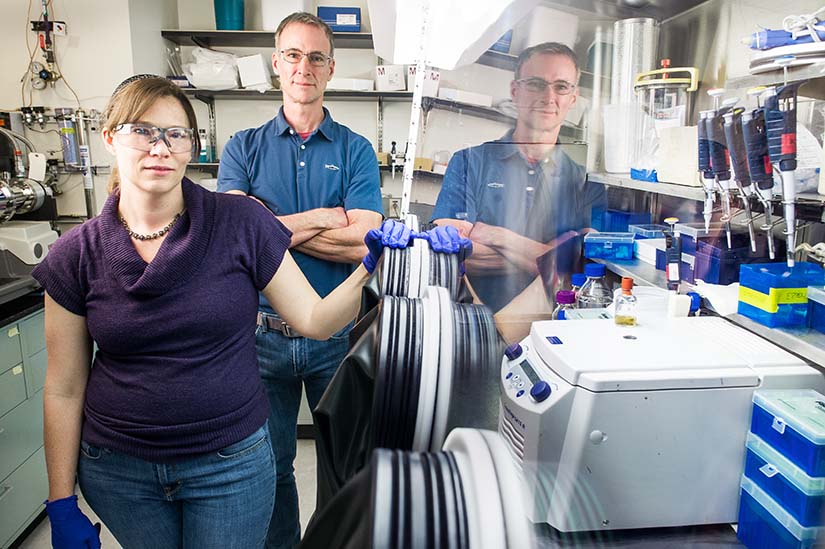 Two NREL researchers next to an anaerobic glove box used to keep sensitive samples in an air free environment.
