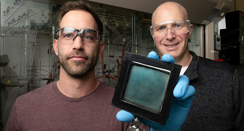 Photo of two males in a laboratory, with one holding a small square sample of a SwitchGlaze glass.