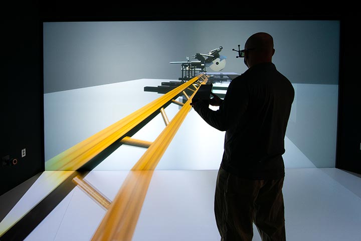 A man stands in front of a digital screen displaying a simulated construction environment.