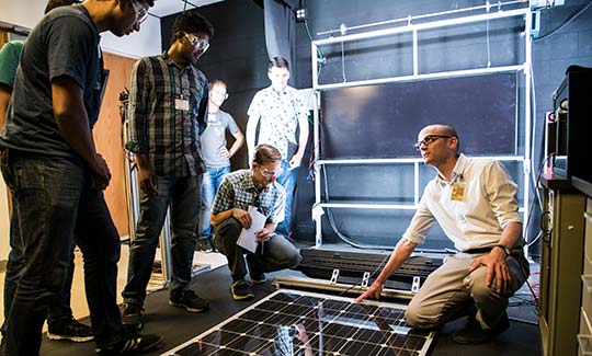 Graduate students participating in the Hands-On PV Experience (HOPE) workshop work with NREL scientist Tim Silverman taking measurements and characterizations of 3-5 and crystalline silicon PV modules in the lab.
