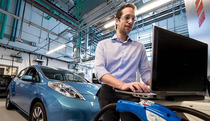 A researcher typing on a computer attached to a plug-in electric vehicle.