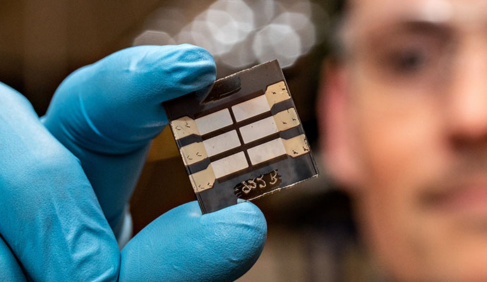 A researcher holding a thin-film solar cell between a thumb and forefinger.
