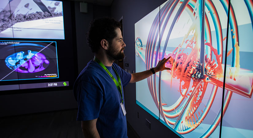Person touching a simulated wind turbine image on a visualization display wall with other data visualizations on another wall
