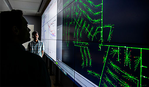 Two researchers view a data visualization display of a multi-timescale simulation for evaluating real-time grid control challenges.