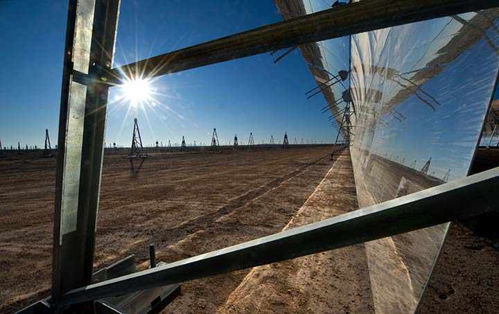 A reflective parabolic trough from the side as the sun gleams further downfield.