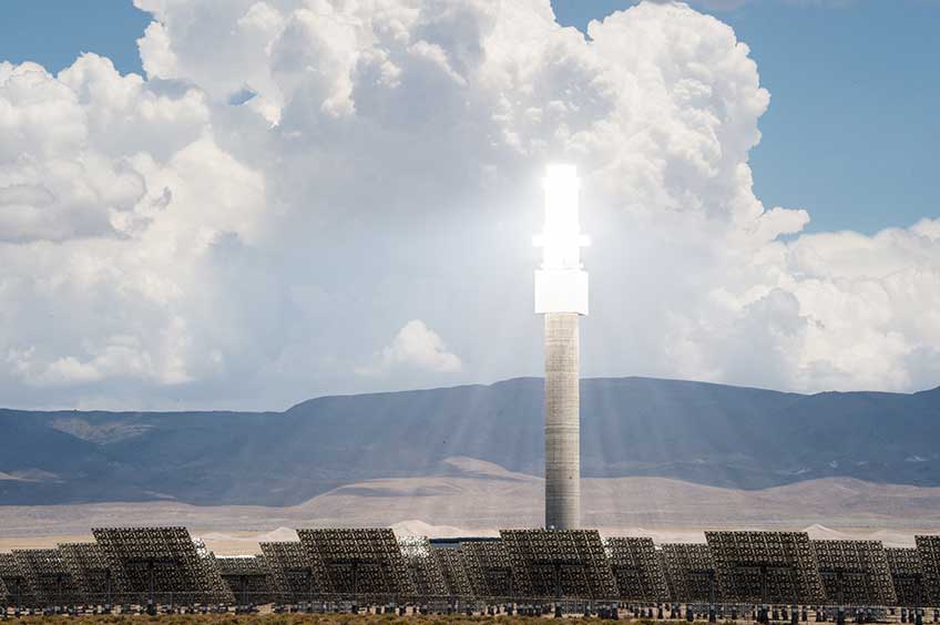 A heliostat glows in front of distant mountains.