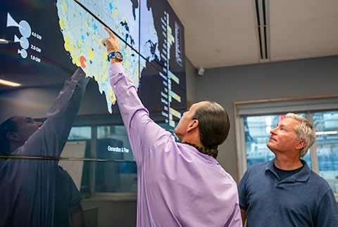 Two people examining map of United States on giant display monitor.