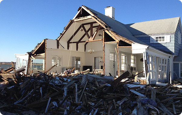 Image of a pile of debris in front of a house with one wall missing.