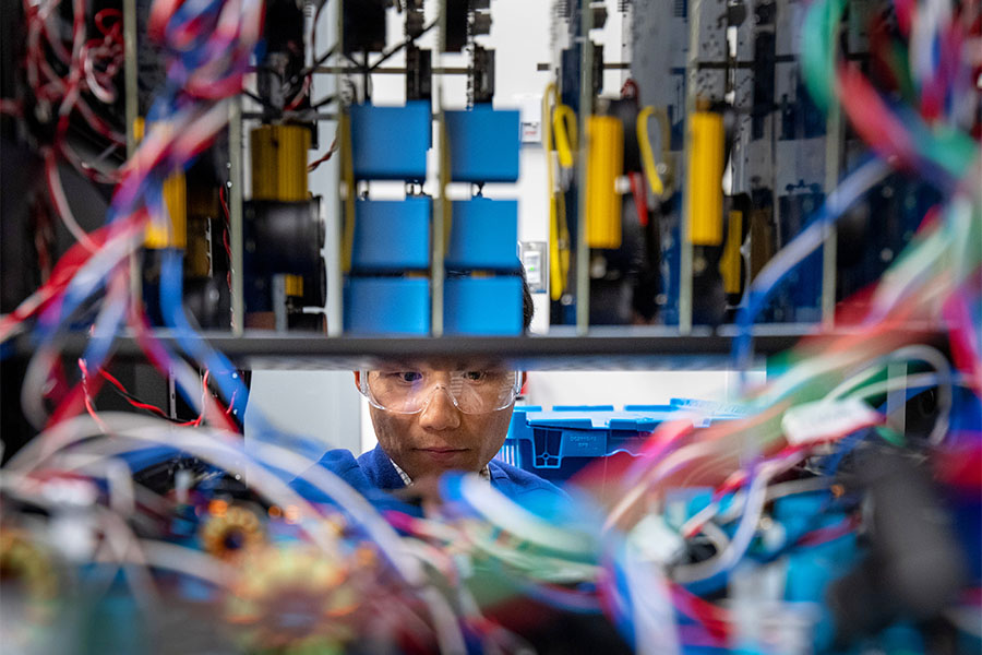 Electrical engineer works in the inverter research area inside a facility looking at grid-forming inverter wires.