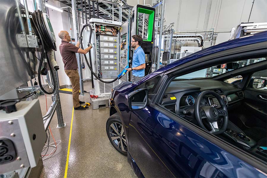 Two people work inside research facility and plug in electric vehicle to high-power charging unit.