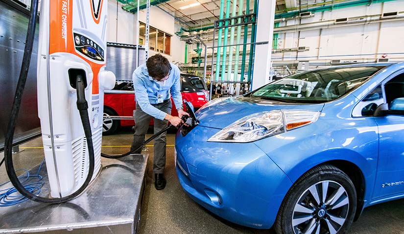 Photo of a researcher plugging in an electric vehicle in a laboratory in the ESIF.