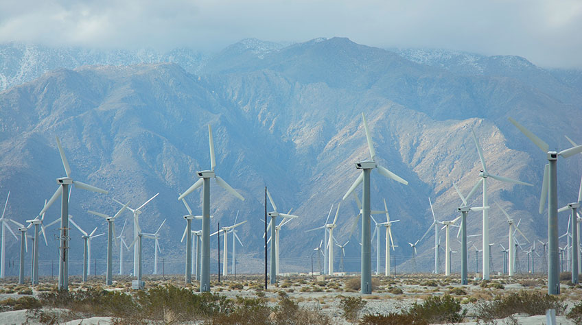 Photo of a group of wind turbines in front of mountains in the California desert.