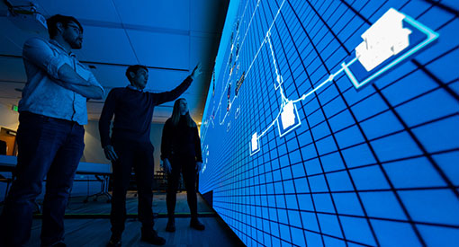 People standing in front of large data screen pointing.