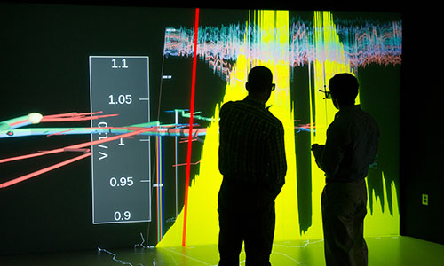 Two people look at bar graph data presented on large screen.