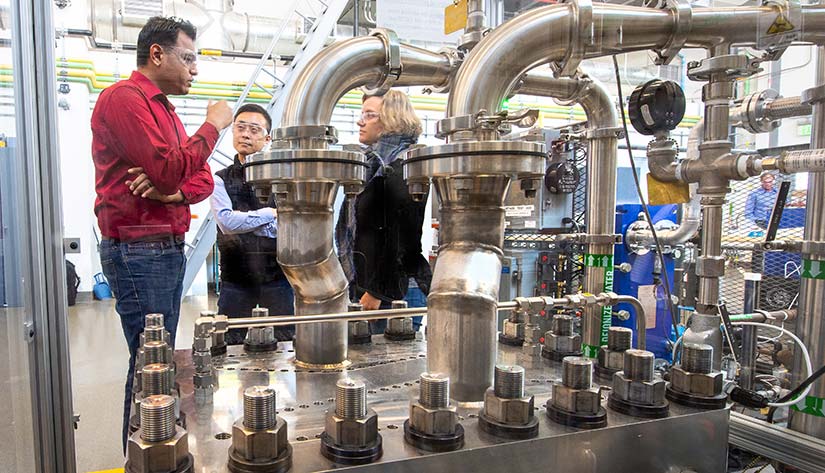 Photo of three researchers talking while looking at a hydrogen electrolyzer.