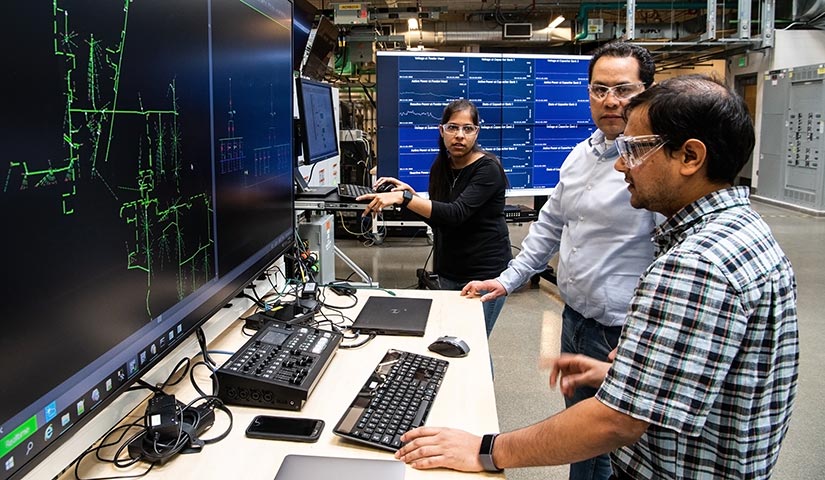 Three researchers looking at and discussing data on computer monitors in a laboratory.
