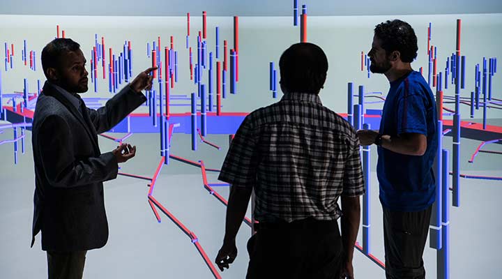 Photo of three researchers looking at a 3D visualization of data on a large screen at the Insight Center Visualization Laboratory in the ESIF.