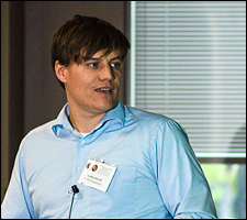 A photo of a young man wearing a light blue shirt using a pointer to show something on a presentation.