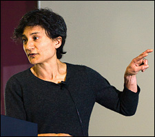 A photo of a woman dressed in black with short hair pointing to a presentation.