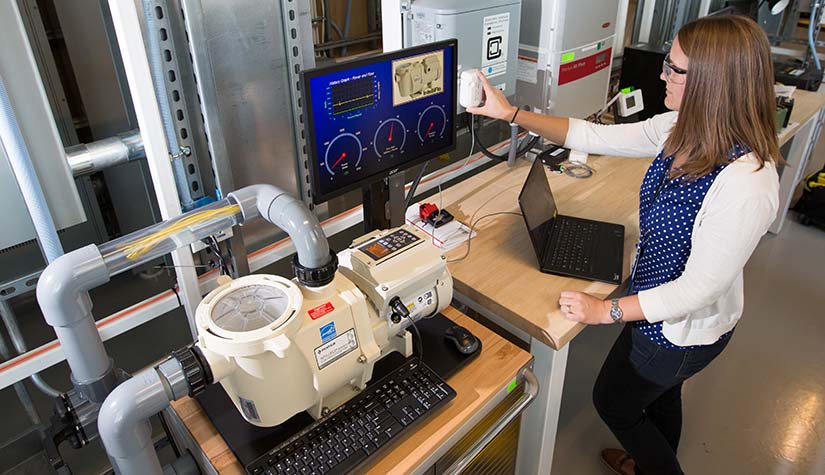 Photo of an NREL researcher working with a communicating pool pump that can adjust its speed to provide grid services.