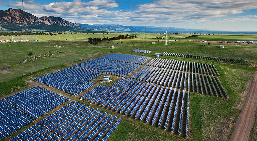 PV panels and a wind turbine near mountain foothills.