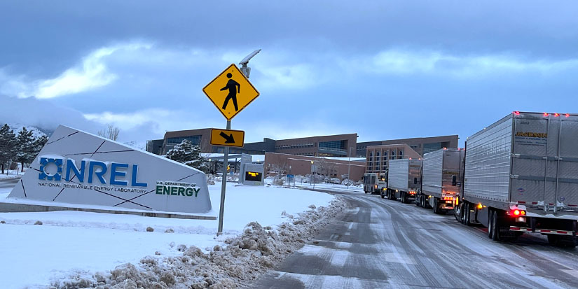 Semi trucks lined up on a snowy road at the NREL main gate.
