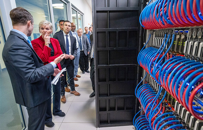 People talk standing next to cables and computer racks inside a computing center.