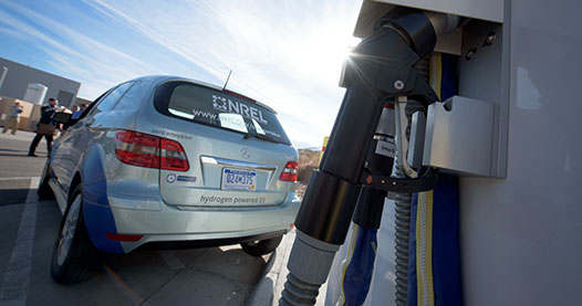 Photo of a fuel cell electric vehicle next to a hydrogen fueling station