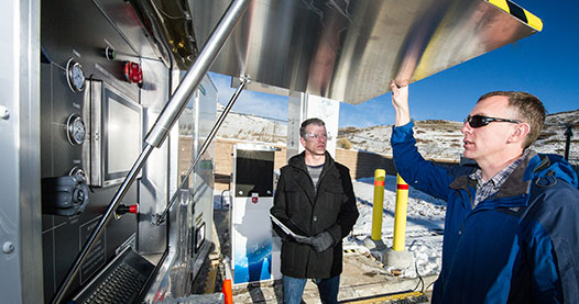 Photo of two researchers looking at a device that measures the performance of hydrogen station equipment