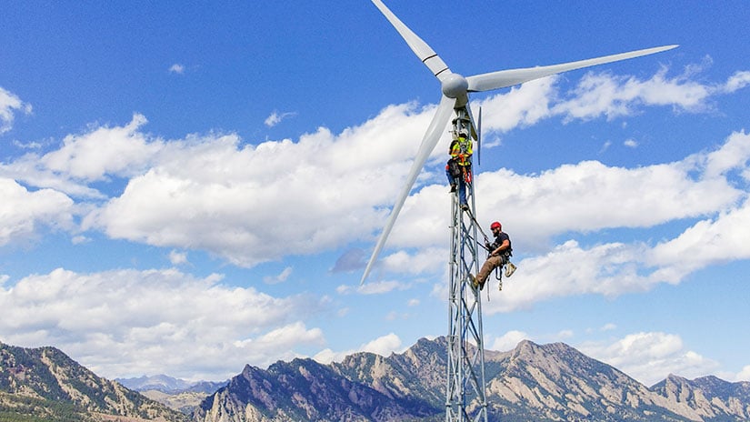 20240228-newsletter-bergey-installation Two people climb a wind turbine with mountains in the background.