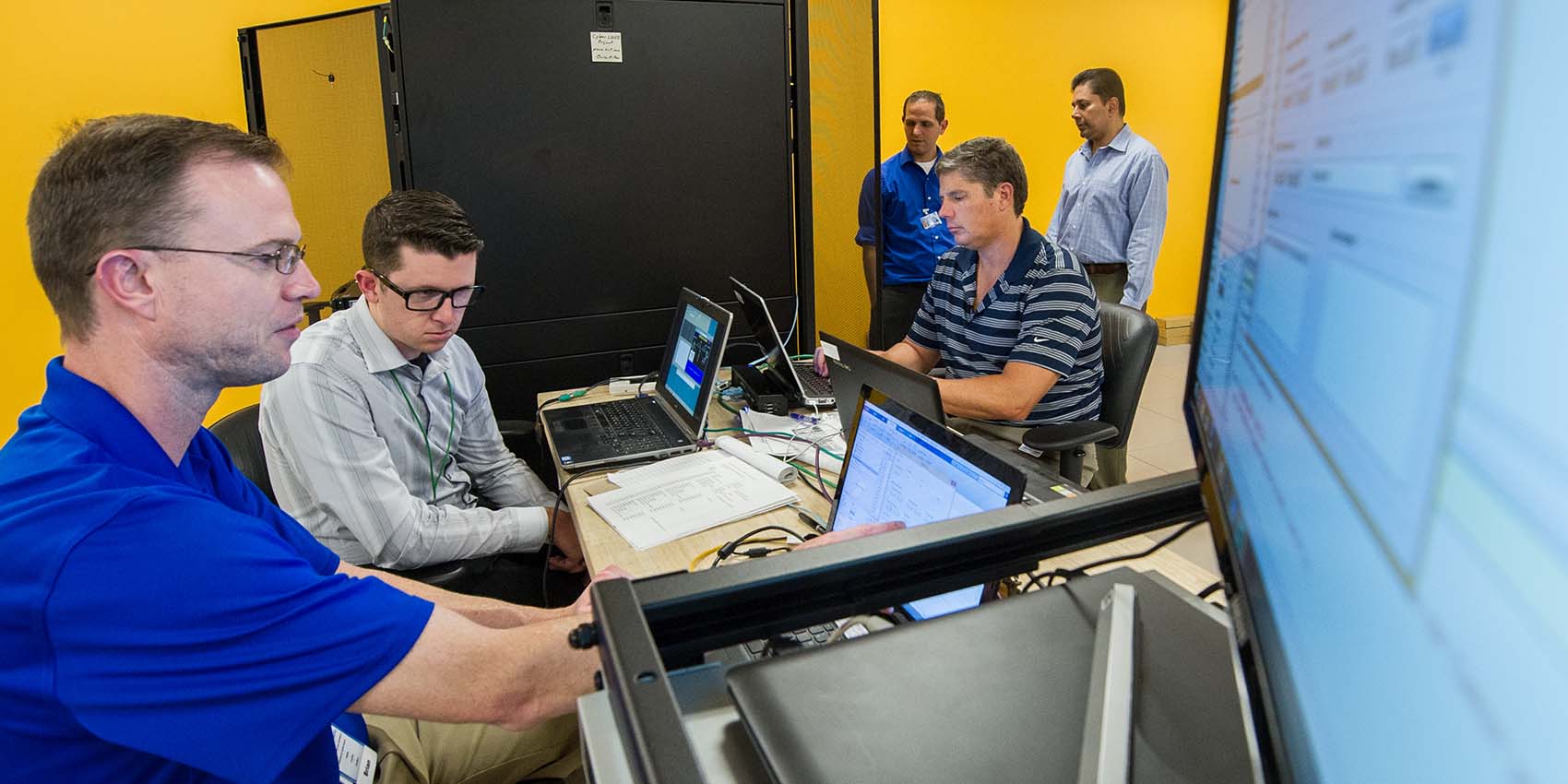adms-34505 People work on a Secure Distribution Grid Management testbed for cyber security in power systems.