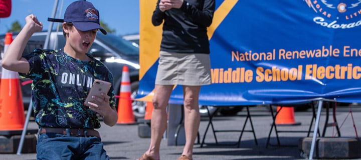 A child pumps a fist in the air while holding a cellphone and kneeling.