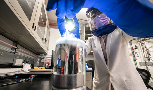 a researcher with safety glasses and a lab coat working on equipment in a lab