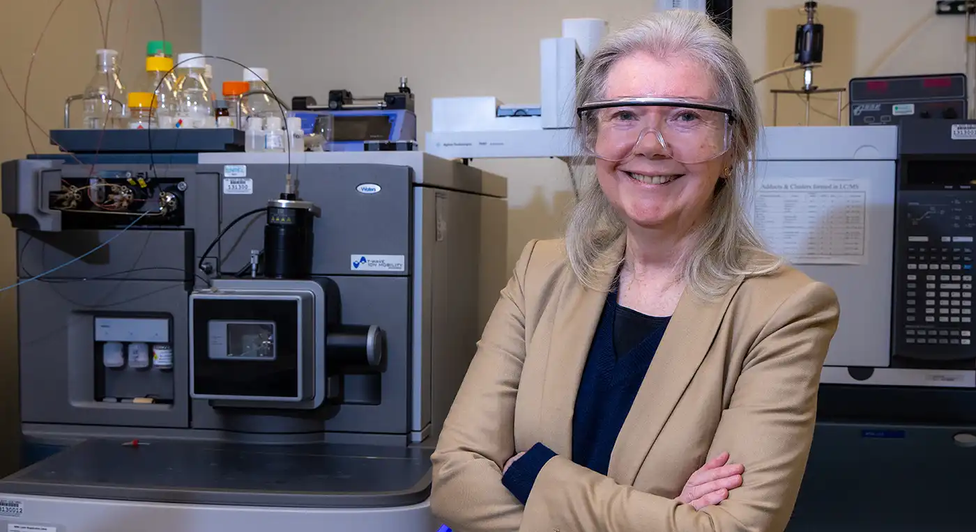 A person wearing safety goggles poses with their arms crossed in a lab.