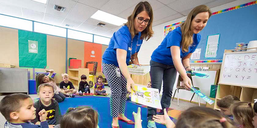 44645 Two NREL staff members hand out books to children in a classroom.