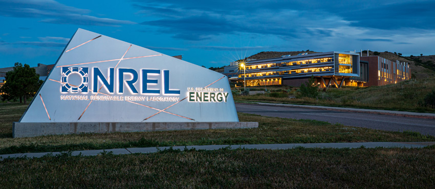 golden-campus-entry-63033 An entryway sign reading NREL - National Renewable Energy Laboratory - U.S. Department of Energy, with a lit-up building behind it.