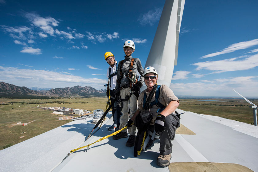 brand-photo-45906 Three people in protective gear pose for a photo atop a wind turbine.