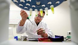 facilities-29191x262 Photo of person in laboratory setting with an array of vials in round holder.