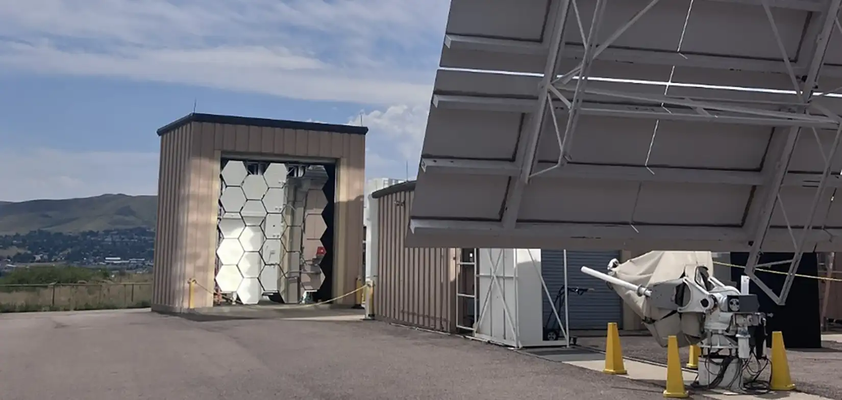 201908-hfsf Photo of the high-flux solar furnace concave mirrors and heliostat in front of a blue sky.
